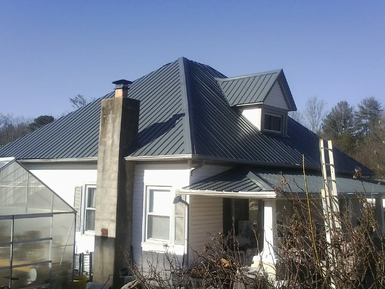 Dark blue standing seam metal roof on a white farmhouse with dormer — Slate & Tile Roof Repair by Roofing Brothers in Craigville