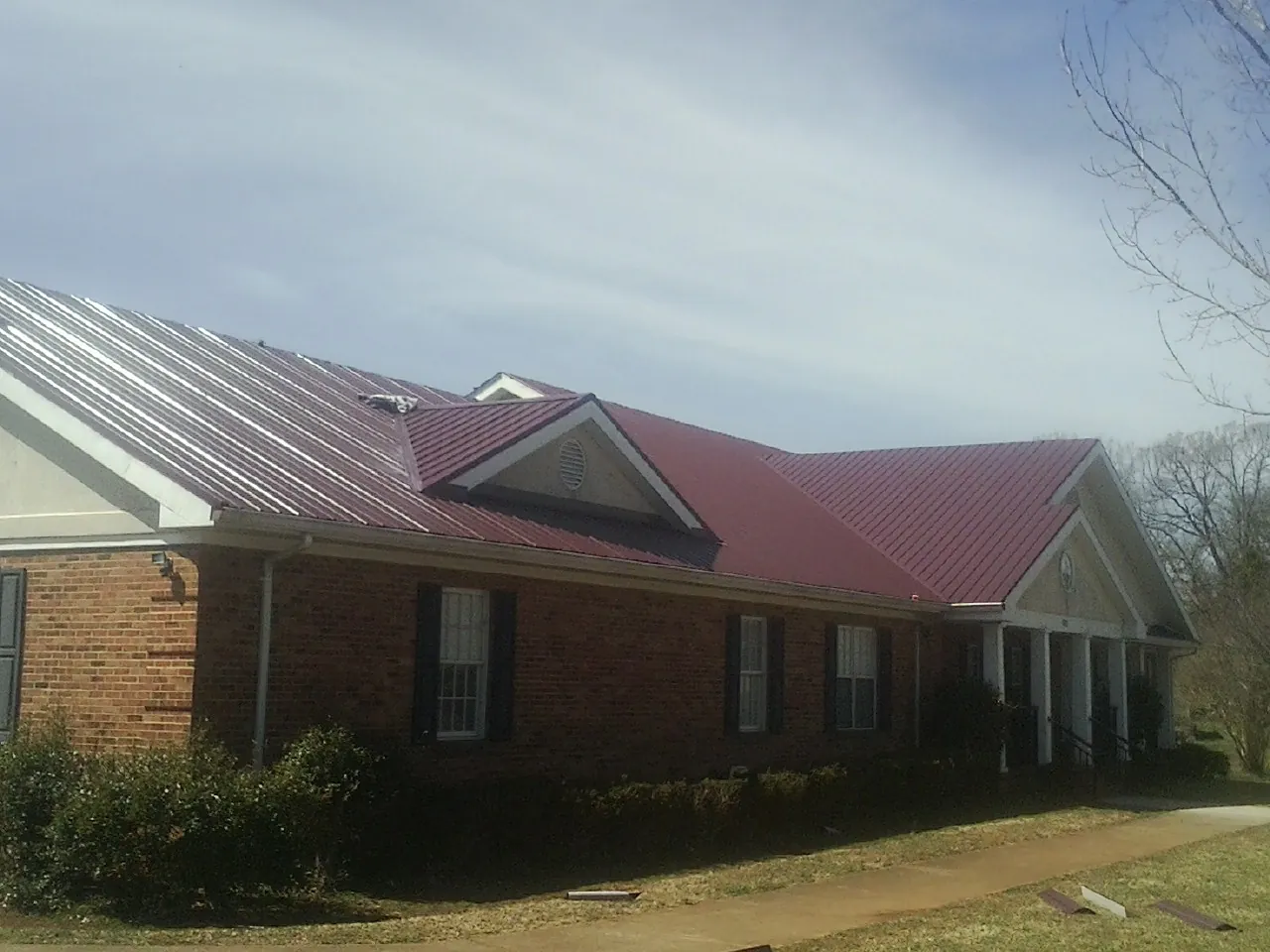 Red metal roof with gabled entries on a long brick building, from a Hail Damage Roof Repair job in Craigville