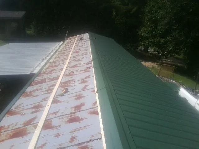 Old rusted panels beside newly installed green metal roofing — Wind Damage Roof Repair by Roofing Brothers in Craigville