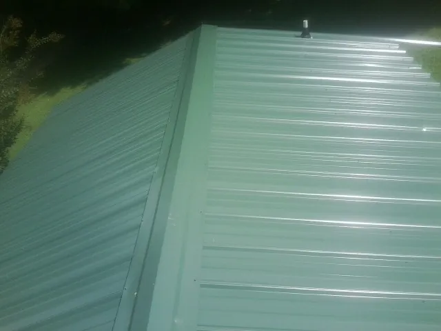 New green metal panels meeting at the ridge of a roof — Flat Roof Repair work by our crew in Craigville