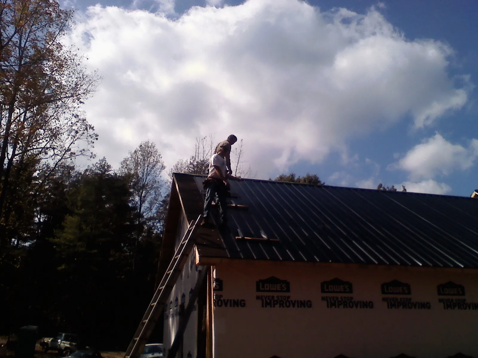 Roofer fastening dark metal panels high against a cloudy sky, from a Roof Inspection job in Craigville