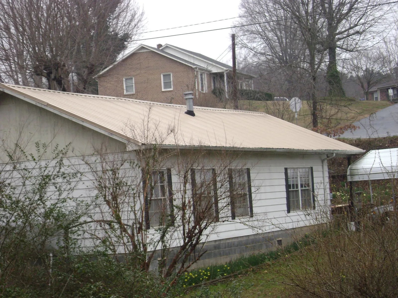 Tan metal roof on a white sided house set into a hillside — Commercial Roofing by Roofing Brothers in Craigville