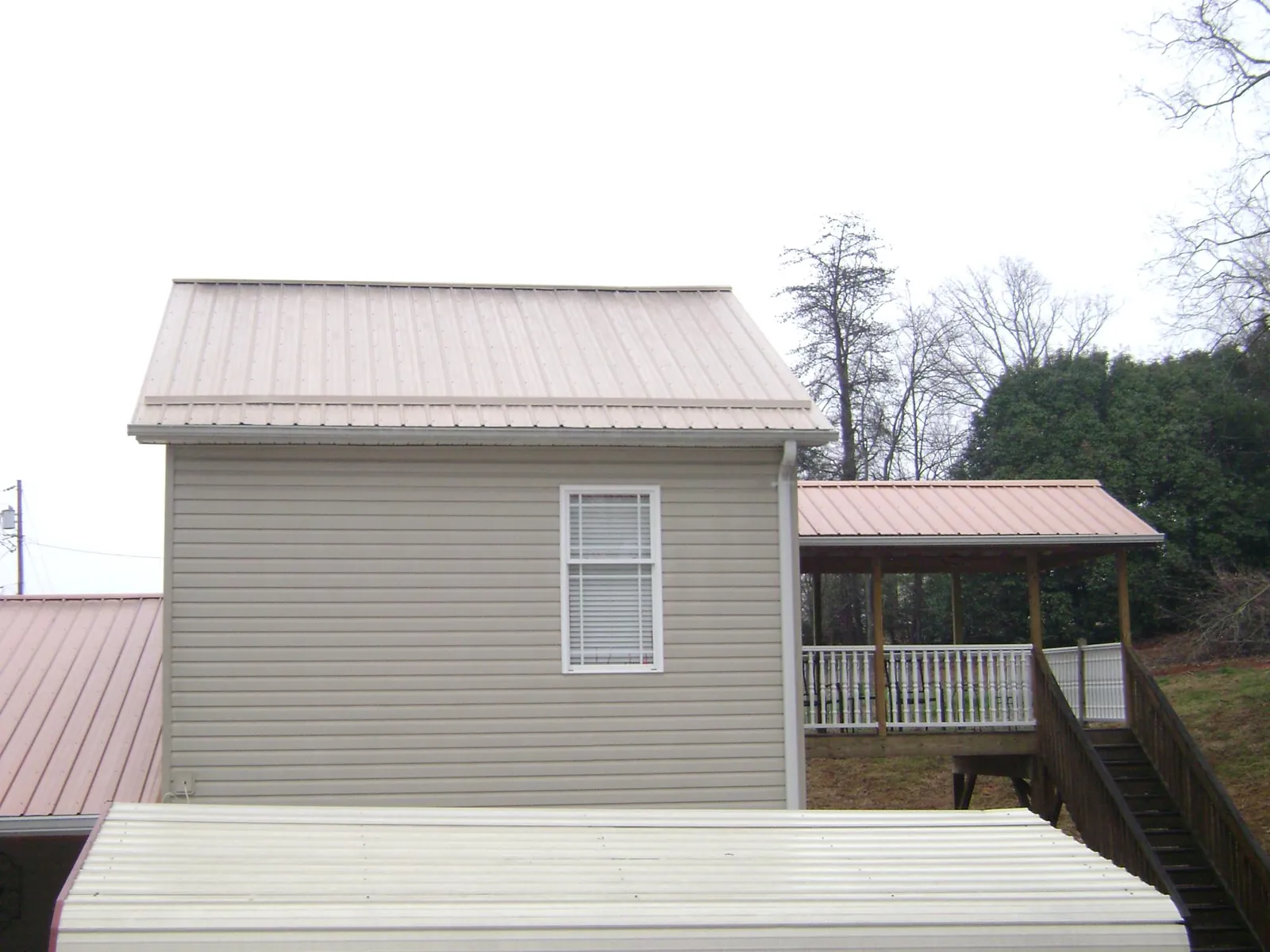 Tan metal roofs on a two story addition and attached porch, from a Roof Replacement job in Craigville